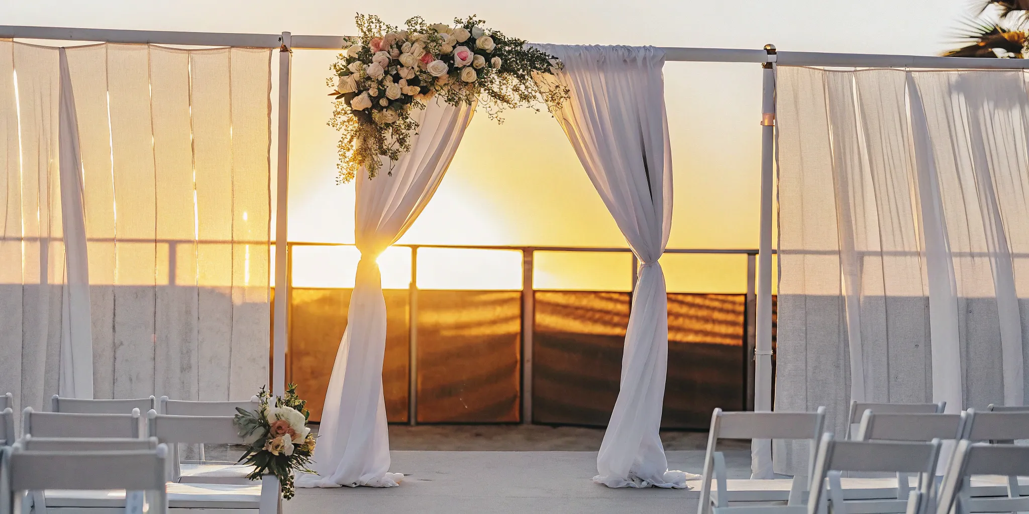California wedding ceremony with floral arch and white chairs.